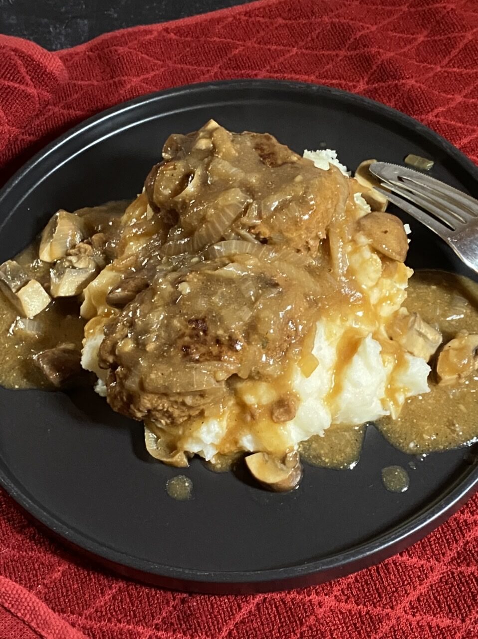 Salisbury steak and gravy over mashed potatoes on a black plate on top of a red towel