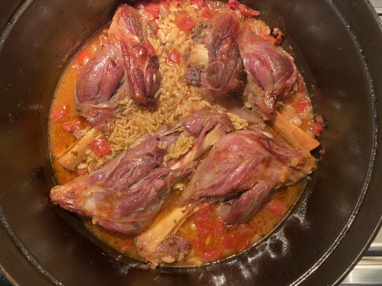 Cooked lamb shank in a Dutch oven with orzo, broth, and tomatoes