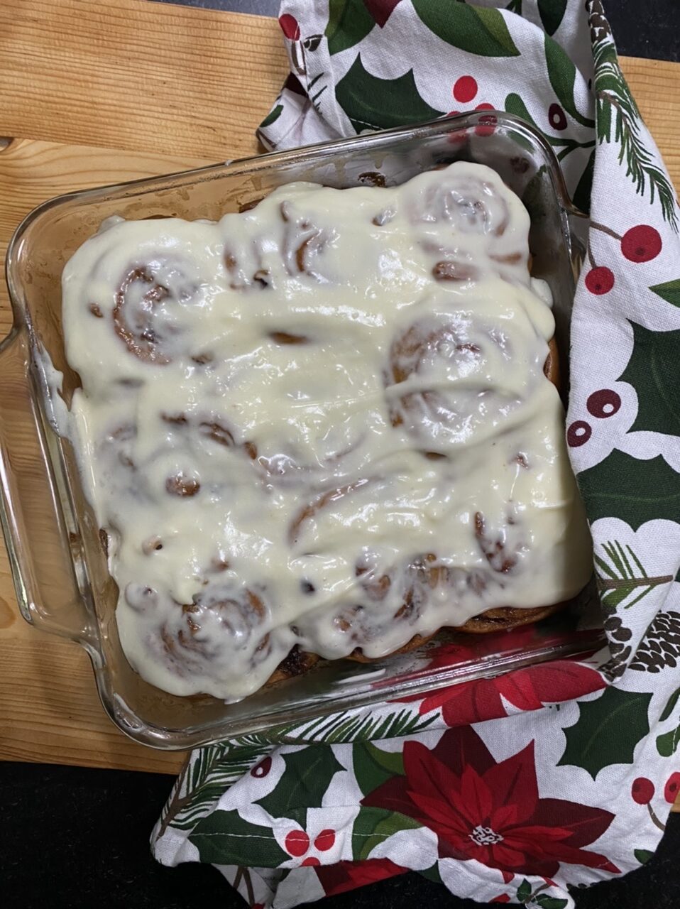 Cinnamon rolls with frosting on top of a wood cutting board and Christmas towel