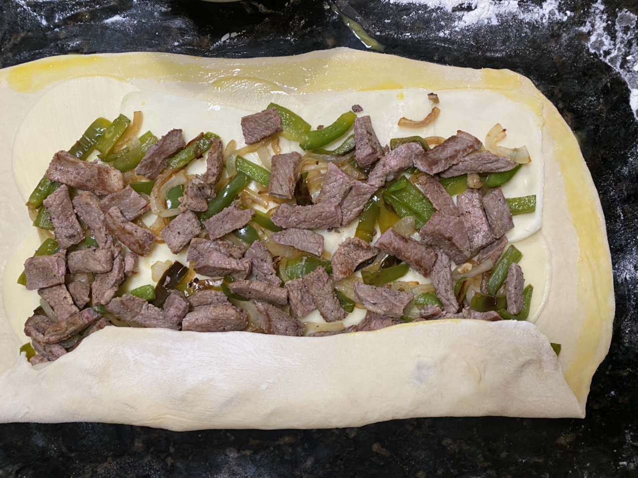 Steak, onions, and peppers on top of pizza dough