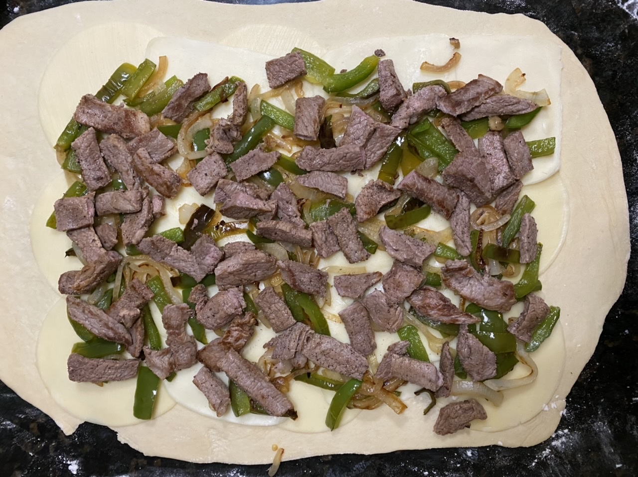 Peppers, onions, and steak on top of pizza dough