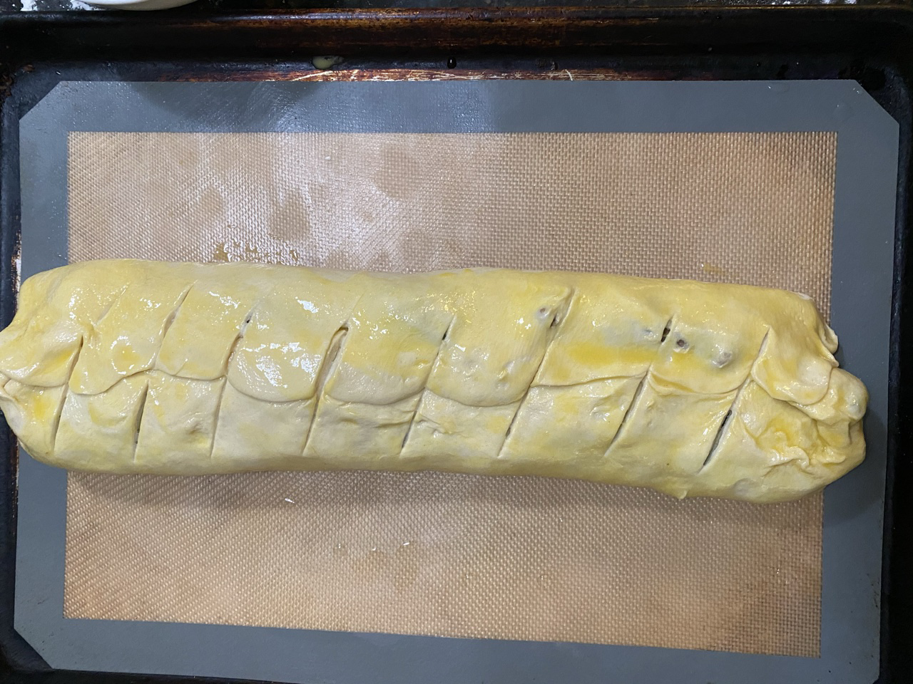 Uncooked philly cheesesteak Stromboli on top of a silicon mat on top of a baking sheet