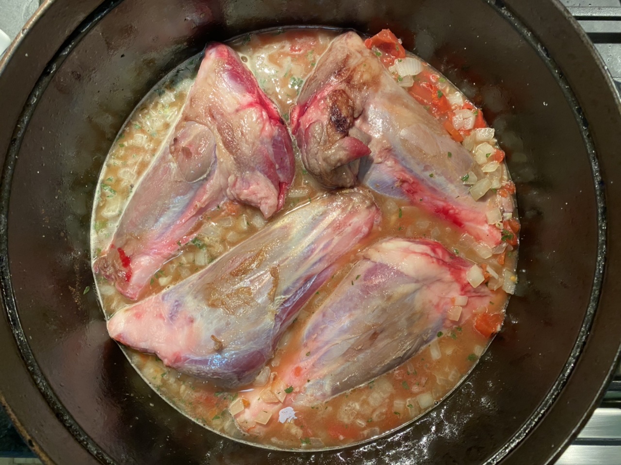 Lamb shank in a Dutch oven with broth, tomatoes and onions