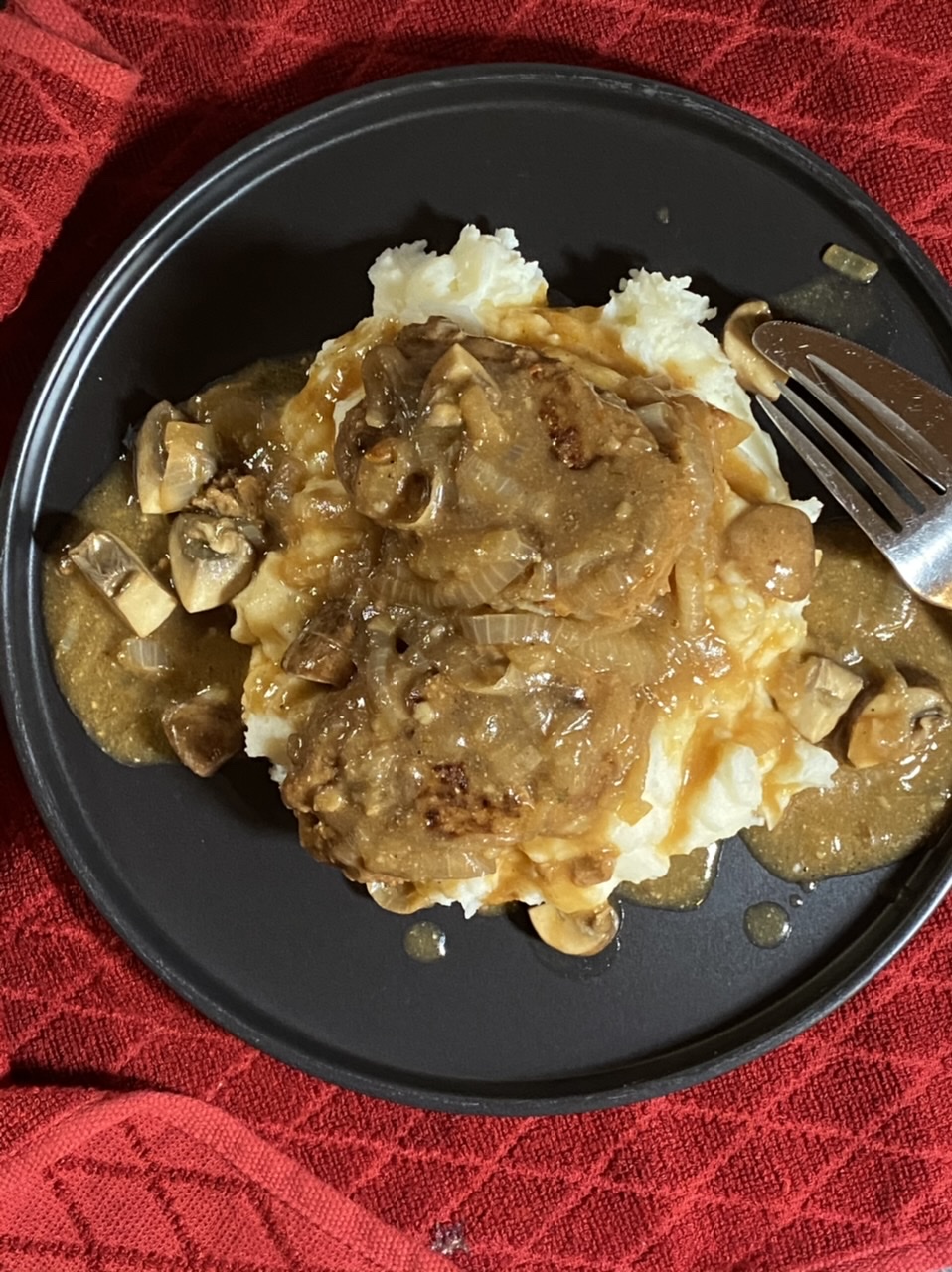 Salisbury steak and gravy over mashed potatoes on a black plate on top of a red towel