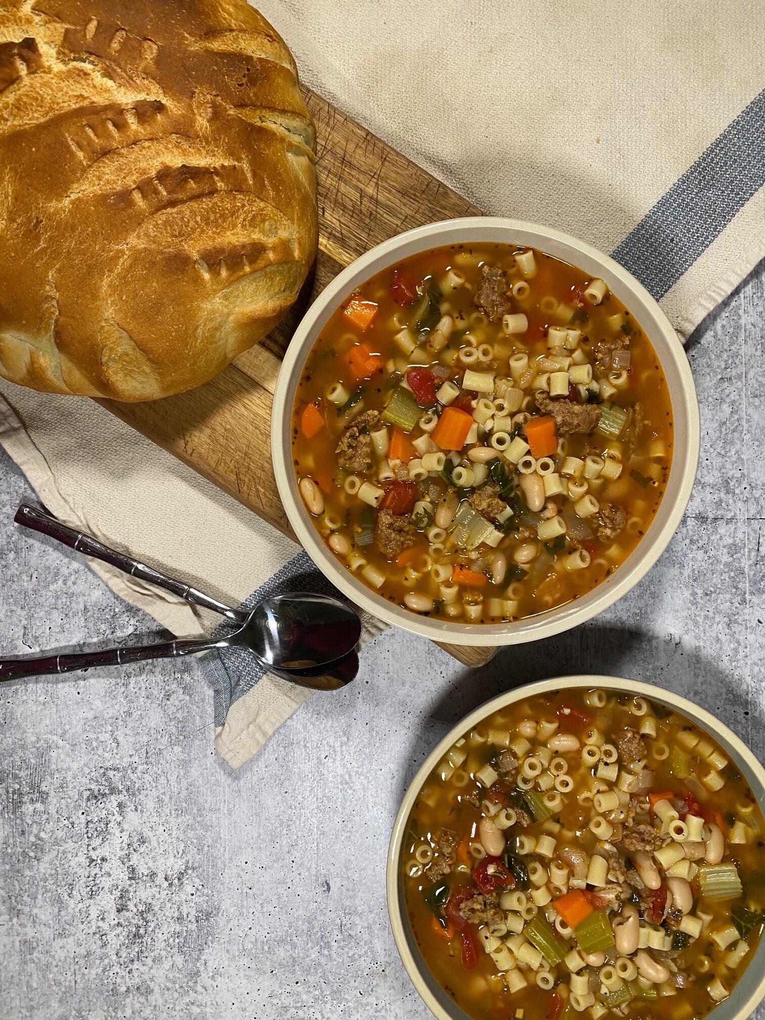 pasta fagioli soup in two bowls on top of a wood cutting board with a loaf of bread