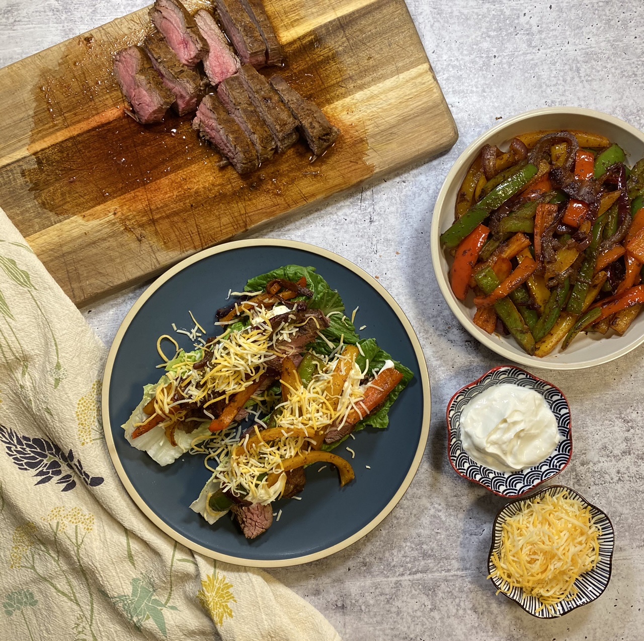 Romaine lettuce flank steak fajitas next to a cutting board of flank steak and a bowl of sautéed vegetables