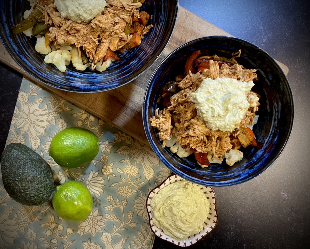 Enchilada chicken bowl in blue bowls on top of a towel next to limes and an avocado
