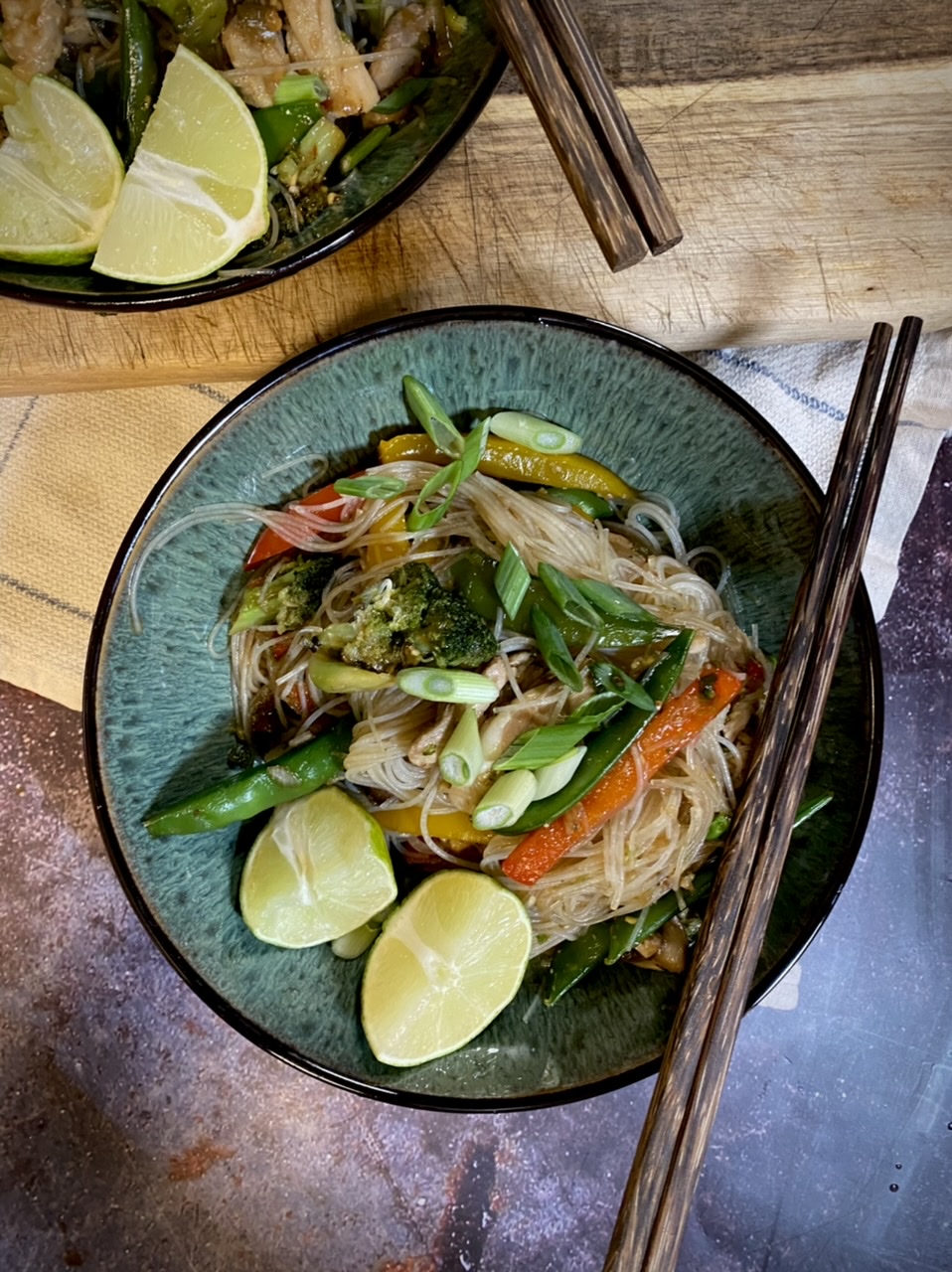 Chicken stir fry in bowls with chopsticks on top of a wooden cutting board