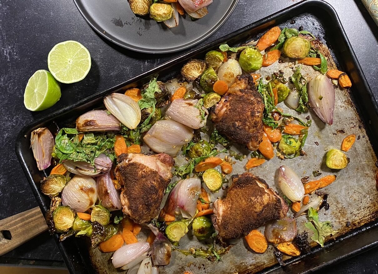 Chicken and vegetables on a baking sheet next to a black plate with chicken and vegetables
