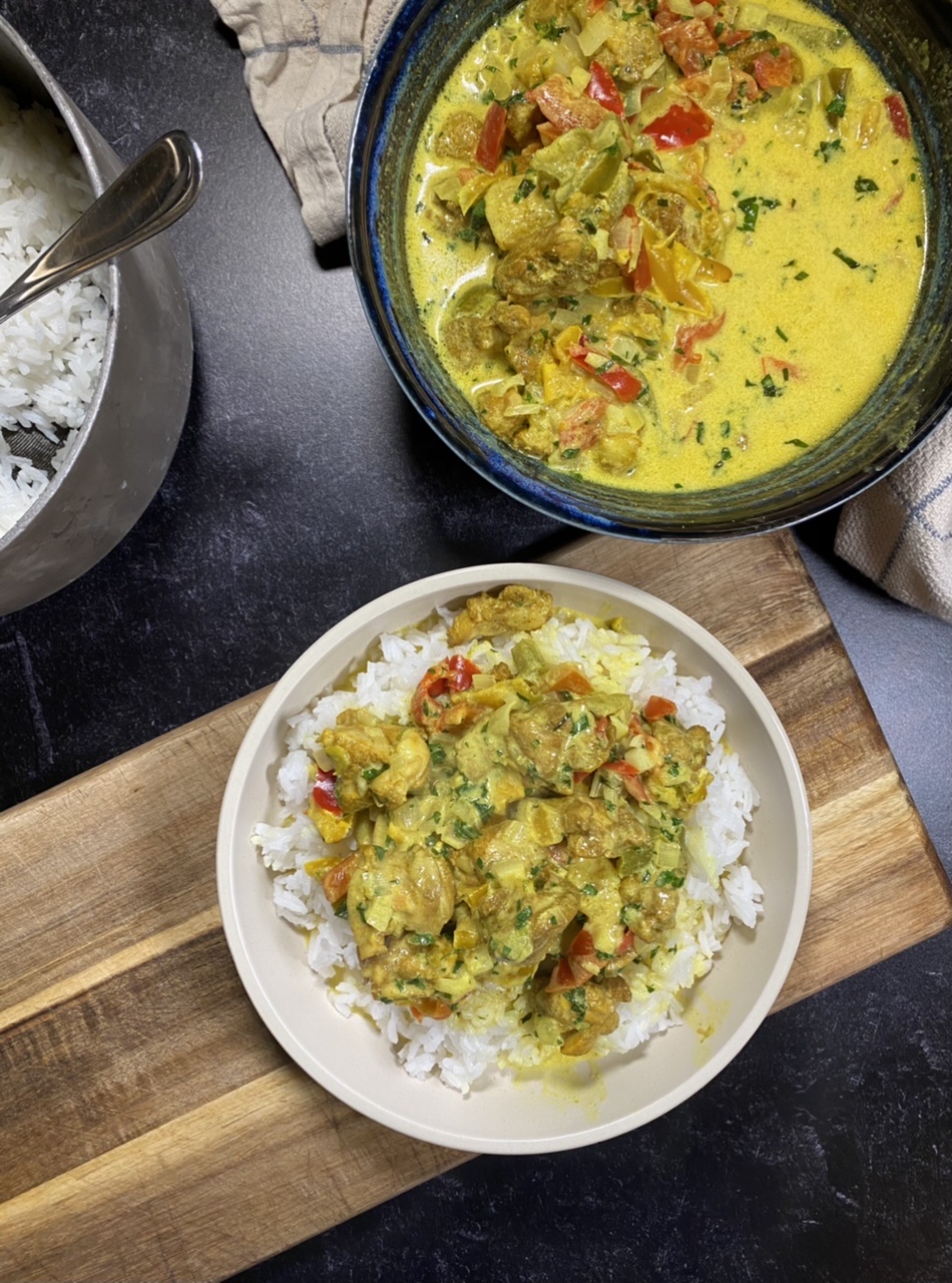 Bowl of Indian coconut curry chicken on top of rice next to a pot of rice and a bowl of coconut curry chicken