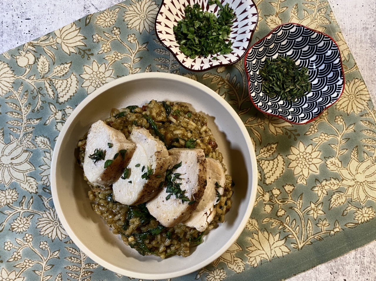 Sun-dried tomato pesto risotto with sliced chicken breast on a wooden cutting board