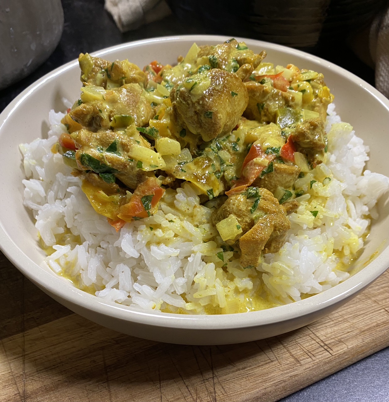 Bowl of Indian coconut curry chicken on top of rice on top of a wooden cutting board