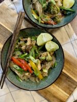 Chicken stir fry in bowls with chopsticks on top of a wooden cutting board