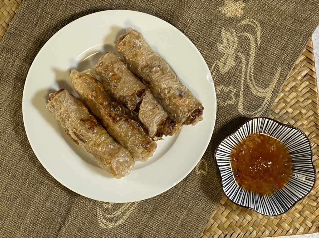 Lumpia on a white plate next to a bowl of dipping sauce