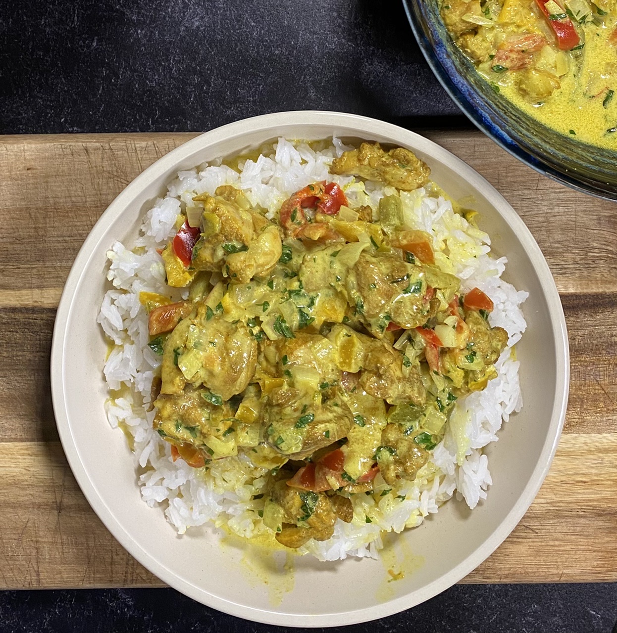 Bowl of Indian coconut curry chicken on top of rice on top of a wooden cutting board