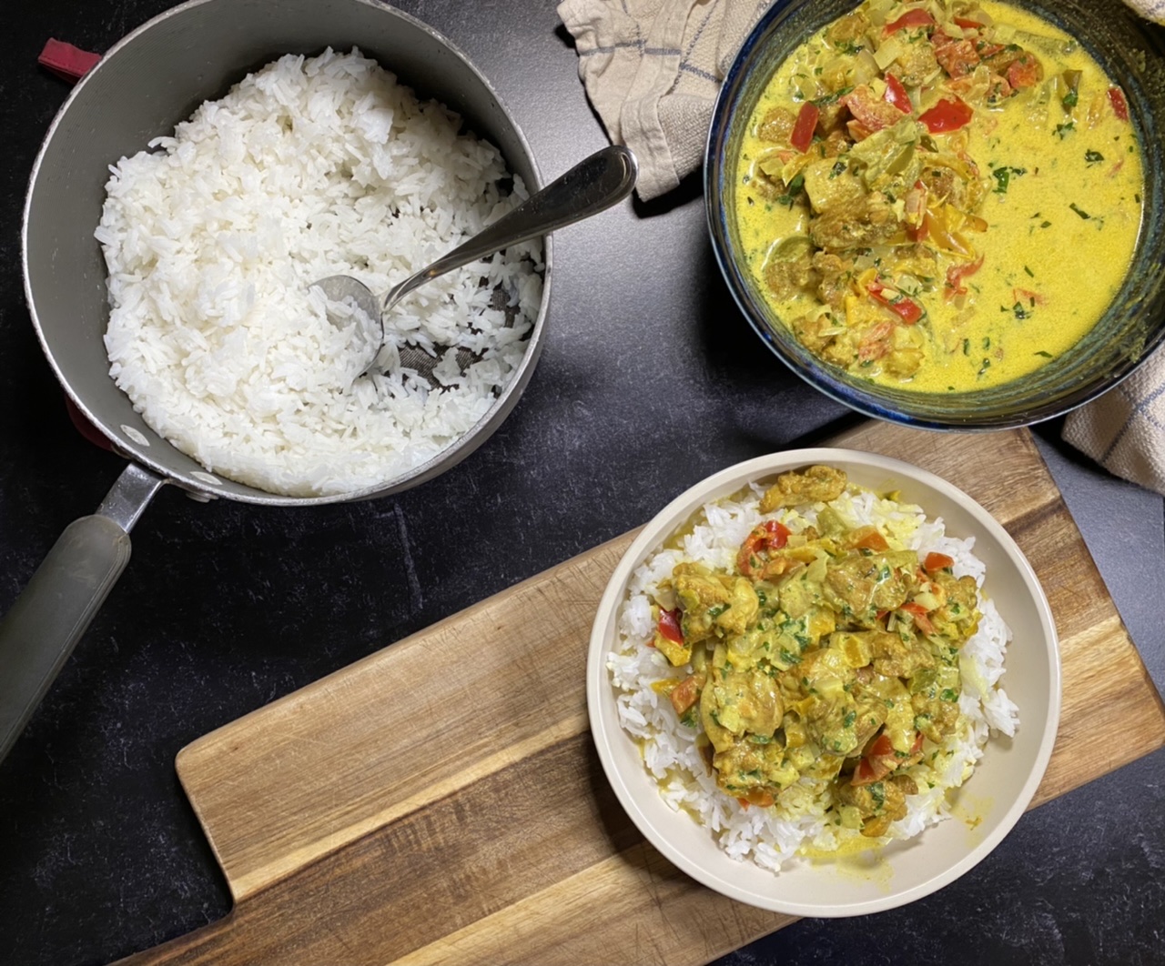 Bowl of Indian coconut curry chicken on top of rice next to a pot of rice and a bowl of coconut curry chicken