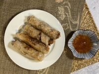 Lumpia on a white plate next to a bowl of dipping sauce