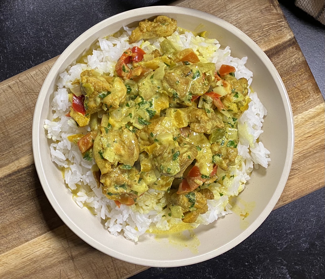 Bowl of Indian coconut curry chicken on top of rice on top of a wooden cutting board