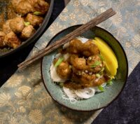 Asian mango chicken meatballs on top of mai fun noodles with mango slices in a blue bowl with wood chopsticks