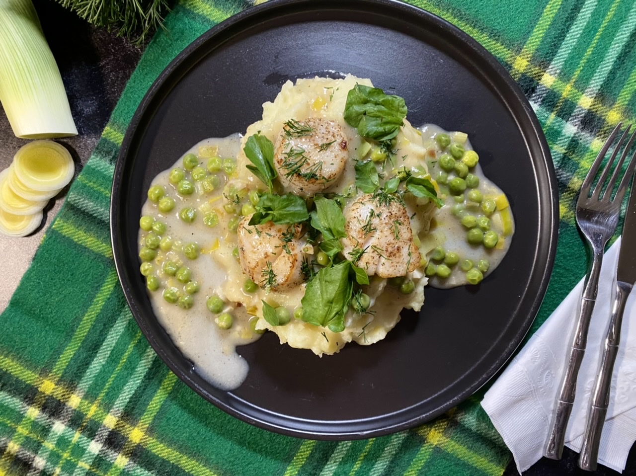 Irish scallops with peas and leeks over mashed potatoes on a black plate