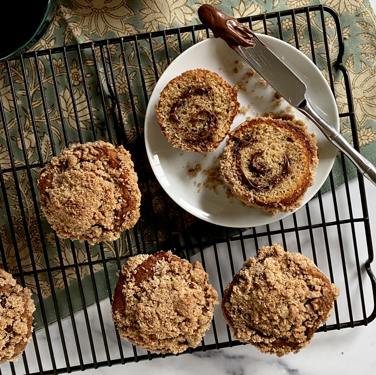 Coffeecake Nutella muffin on a white plate with a knife surrounded by muffins on a wire rack