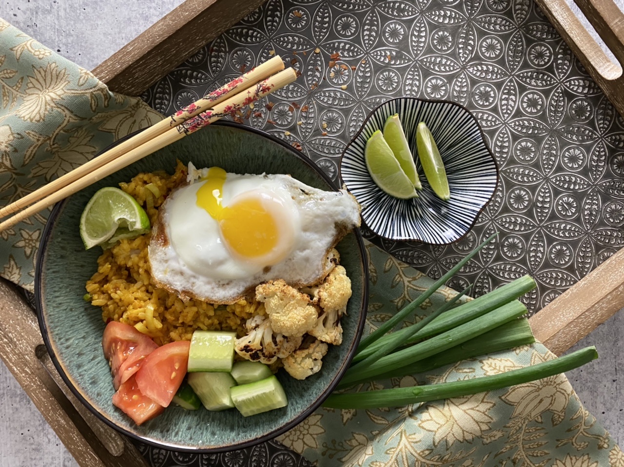 Indonesian fried rice in a green bowl with chop sticks and a fried rice on a serving tray