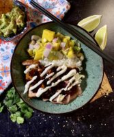 Tuna burrito bowls with wasabi cream and mango salsa in a green bowl next to limes and guacamole