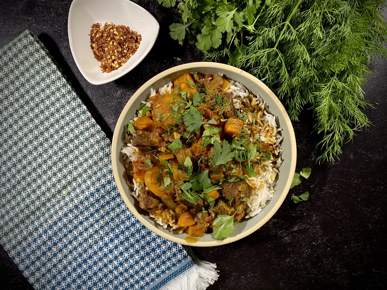Persian lamb stew with apricots and sweet potatoes in a light blue bowl next to fresh dill
