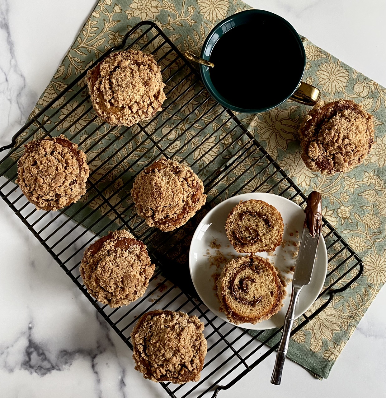 Coffeecake Nutella muffin on a white plate with a knife surrounded by muffins on a wire rack And a cup of coffee