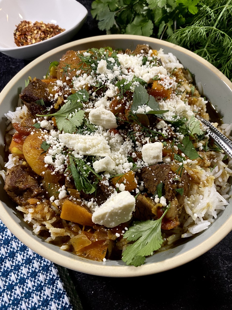 Persian lamb stew with apricots and sweet potatoes in a light blue bowl next to fresh dill