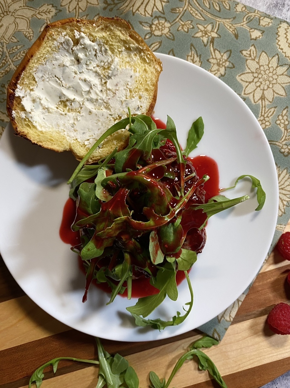 Venison burger with arugula and raspberry sauce on a white plate on top of a cutting board