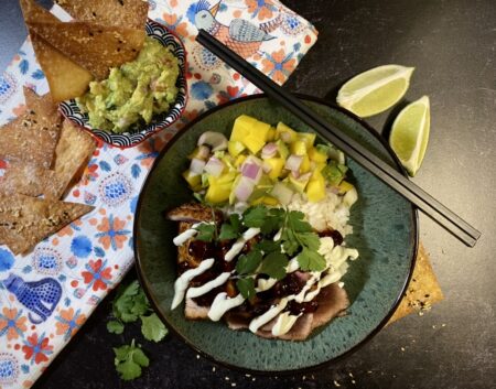 Tuna burrito bowls with wasabi cream and mango salsa in a green bowl next to limes and guacamole