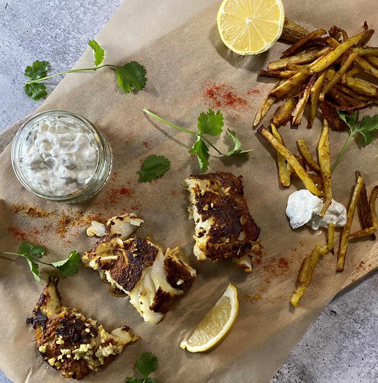 Indian fish and turmeric French fries on parchment paper with tzatziki and lemons