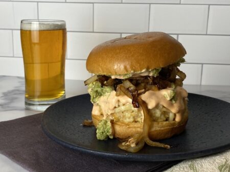 White bean burgers with smashed avocado and caramelized onions on a blue plate with a glass of beer