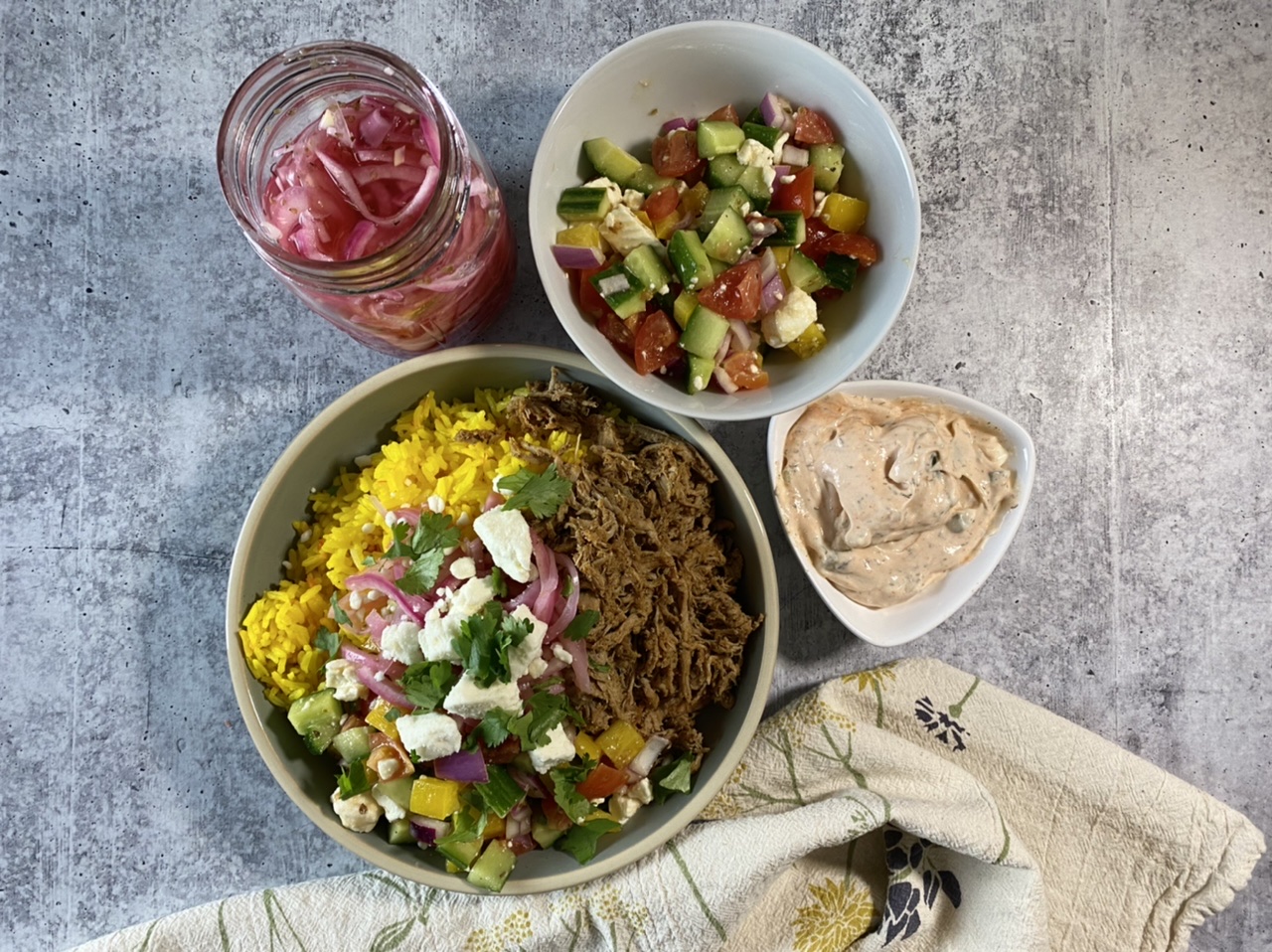 Greek pork gyro and saffron rice bowls next to pickled red onions and Greek salad