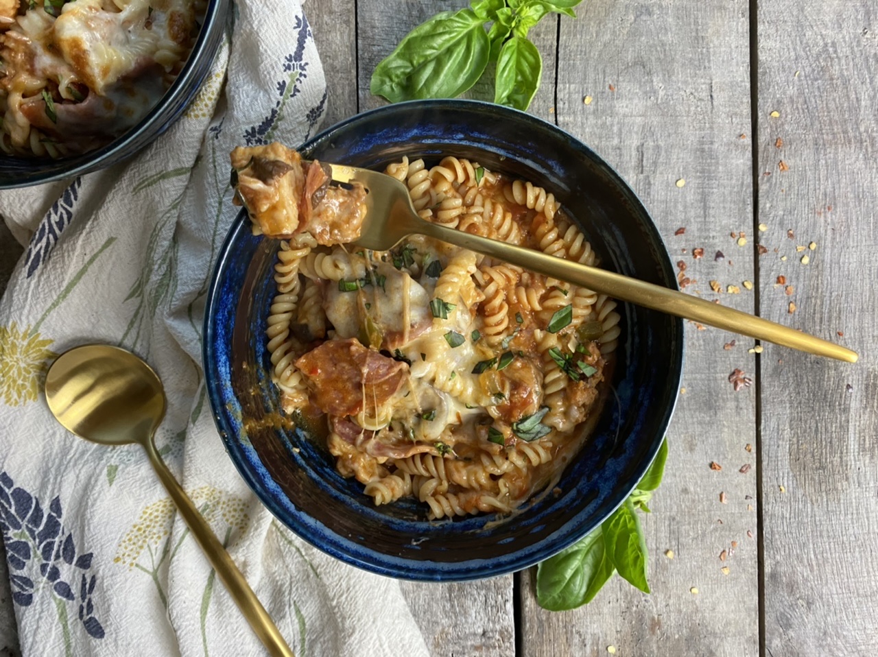 Meat lover’s pizza casserole in a blue bowl with a gold fork with basil on a wood board