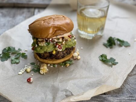 Black bean burger with guacamole and corn salsa next to a glass of whiskey