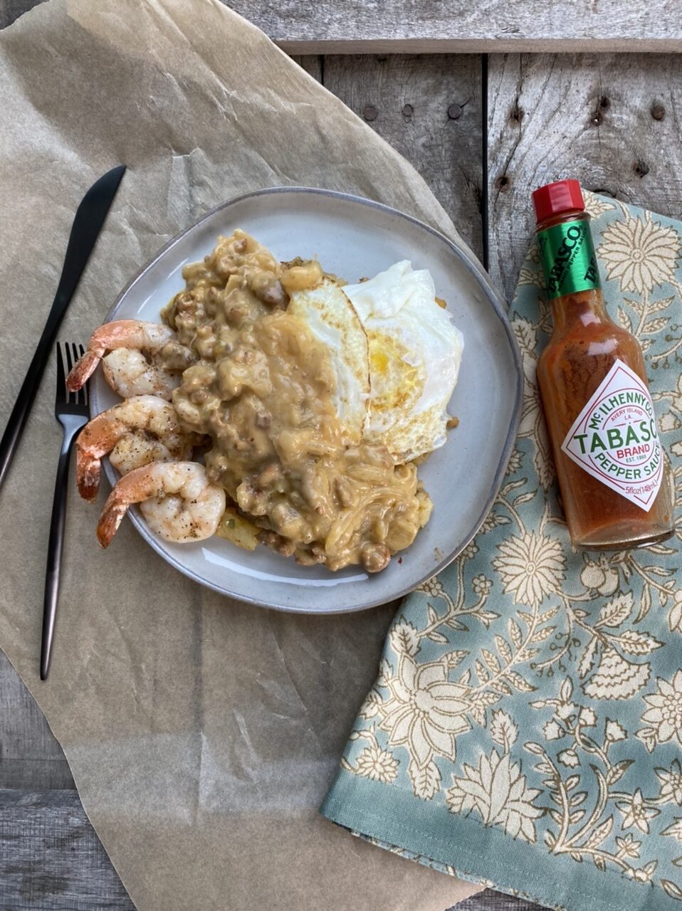 Cajun egg skillet with sausage gravy and shrimp on a white plate next to Tabasco and a hand towel