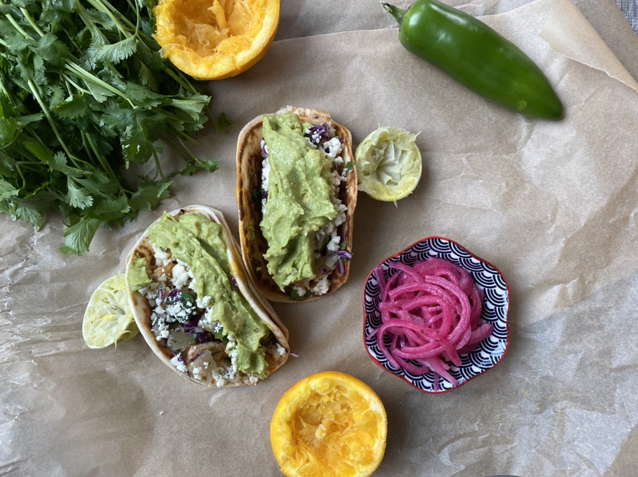 Chipotle pork tacos with pineapple salsa and guacamole with a bowl of pickled red onions, squeezed oranges, and jalapeño