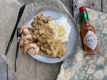 Cajun egg skillet with sausage gravy and shrimp on a white plate next to Tabasco and a hand towel