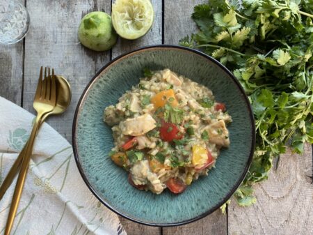Thai green curry risotto in a green bowl next to juiced limes and cilantro