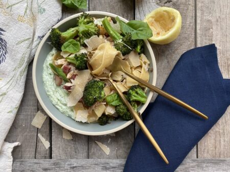 Browned butter pappardelle with roast broccoli and whipped ricotta in a blue bowl next to lemons and gold silverware