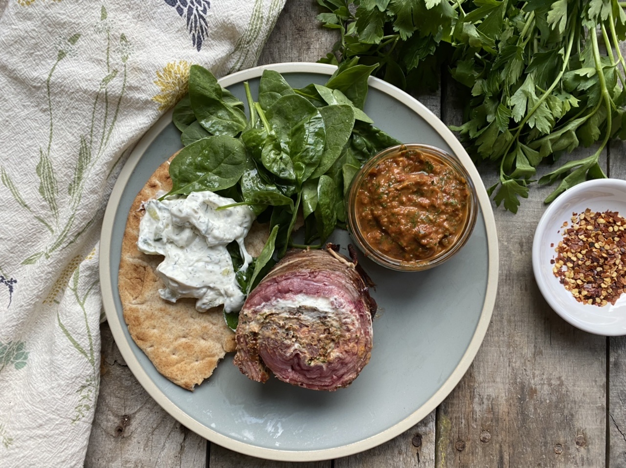 Goat cheese stuffed flank steak with sun-dried tomato chimichurri and flatbread with spinach salad on a blue plate