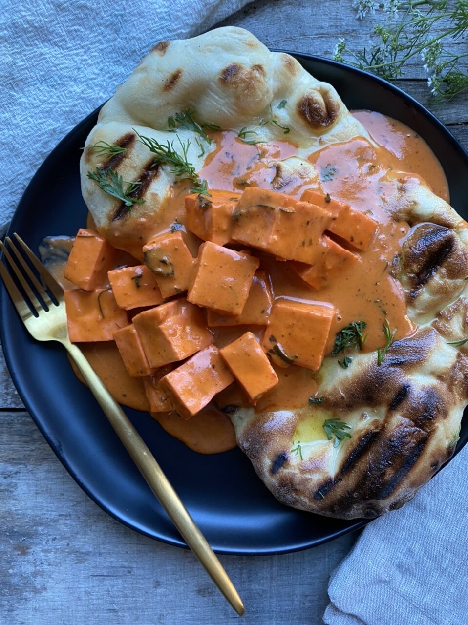 Paneer tikka masala on top of grilled naan on a black plate with a gold fork