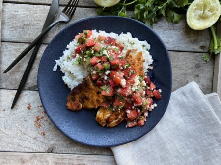 Blackened tilapia with strawberry salsa on coconut rice on a blue plate next to black silverware and cilantro