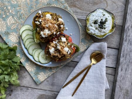 Lebanese mujadara stuffed bell peppers with cucumbers and labneh on a blue plate next to gold silverware and cilantro