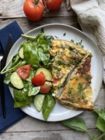 Frittata next to a salad on a white plate next to a blue napkin