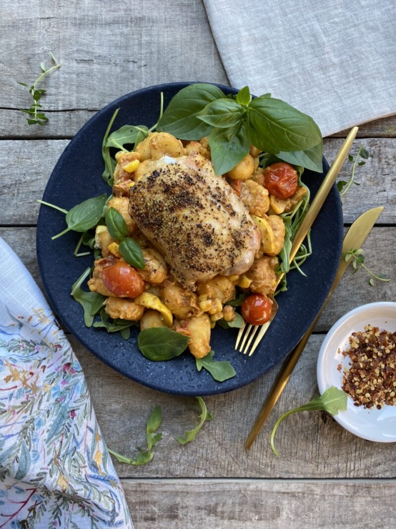 Roasted lemon pepper chicken on roasted gnocchi, cherry tomatoes, yellow squash, and arugula on a blue plate