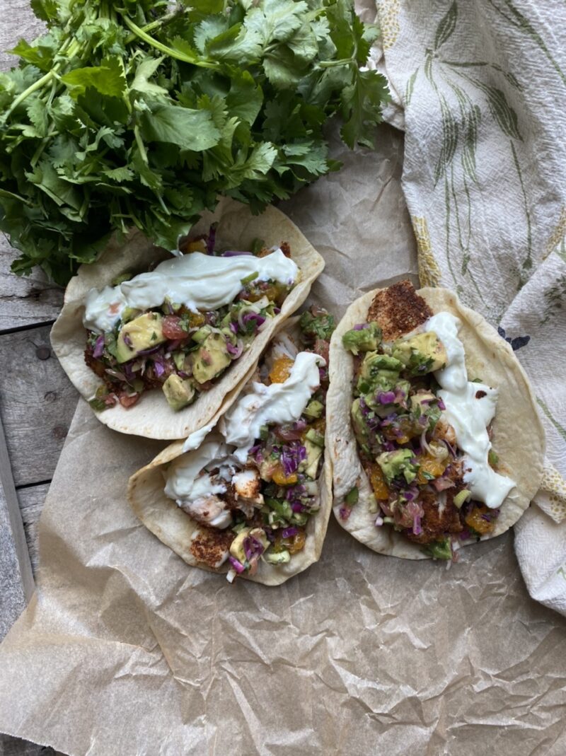 Tilapia tacos with grapefruit citrus salsa on parchment paper next to cilantro